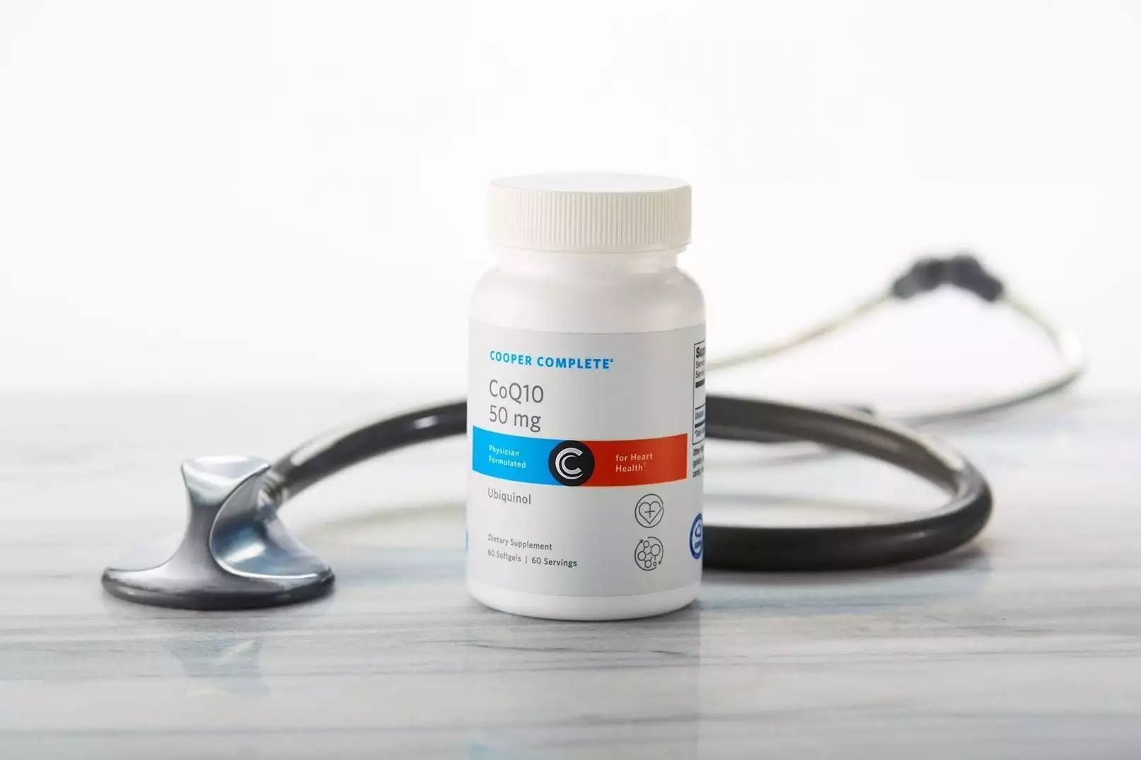 Cooper Complete CoQ10 50mg Ubiquinol dietary supplement bottle on a marble surface with stethoscope