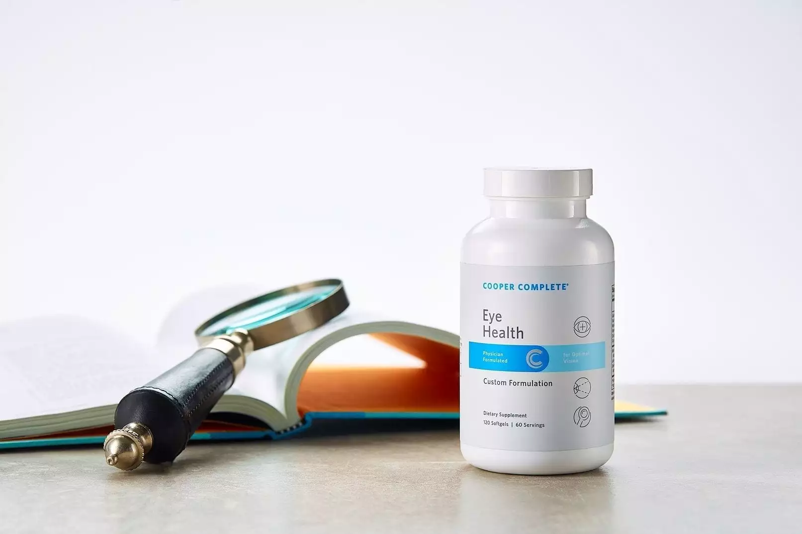 Cooper Complete Eye Health dietary supplement bottle on a tablet along side an open book with magnifying glass