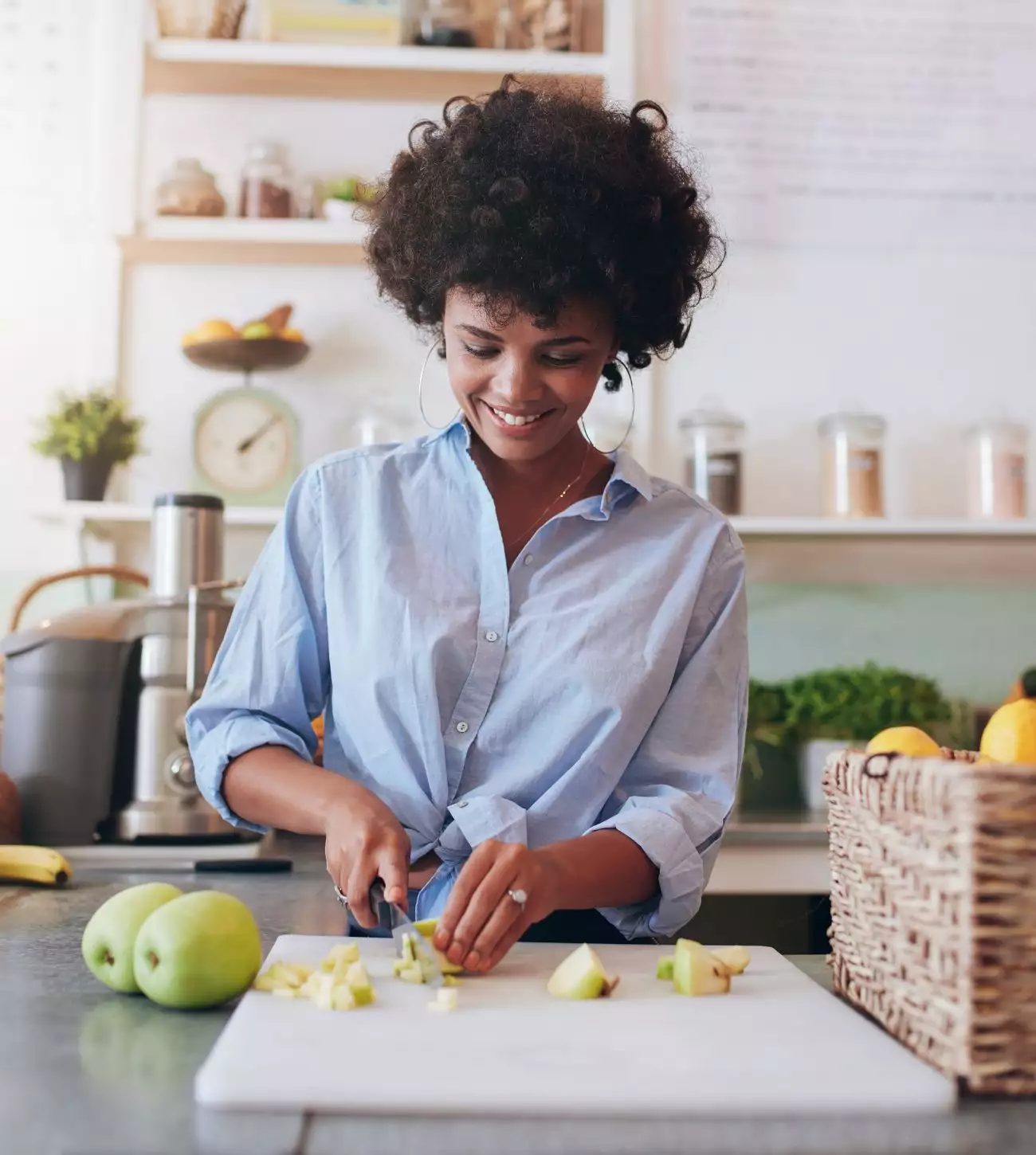 Photo of a young woman cutting green apples on a cutting board in the kitchen.