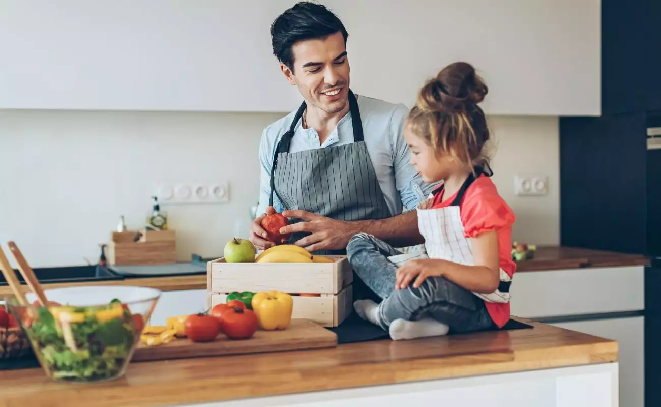 Photo of a young father and daughter prepping fresh vegetables and making a salad together.