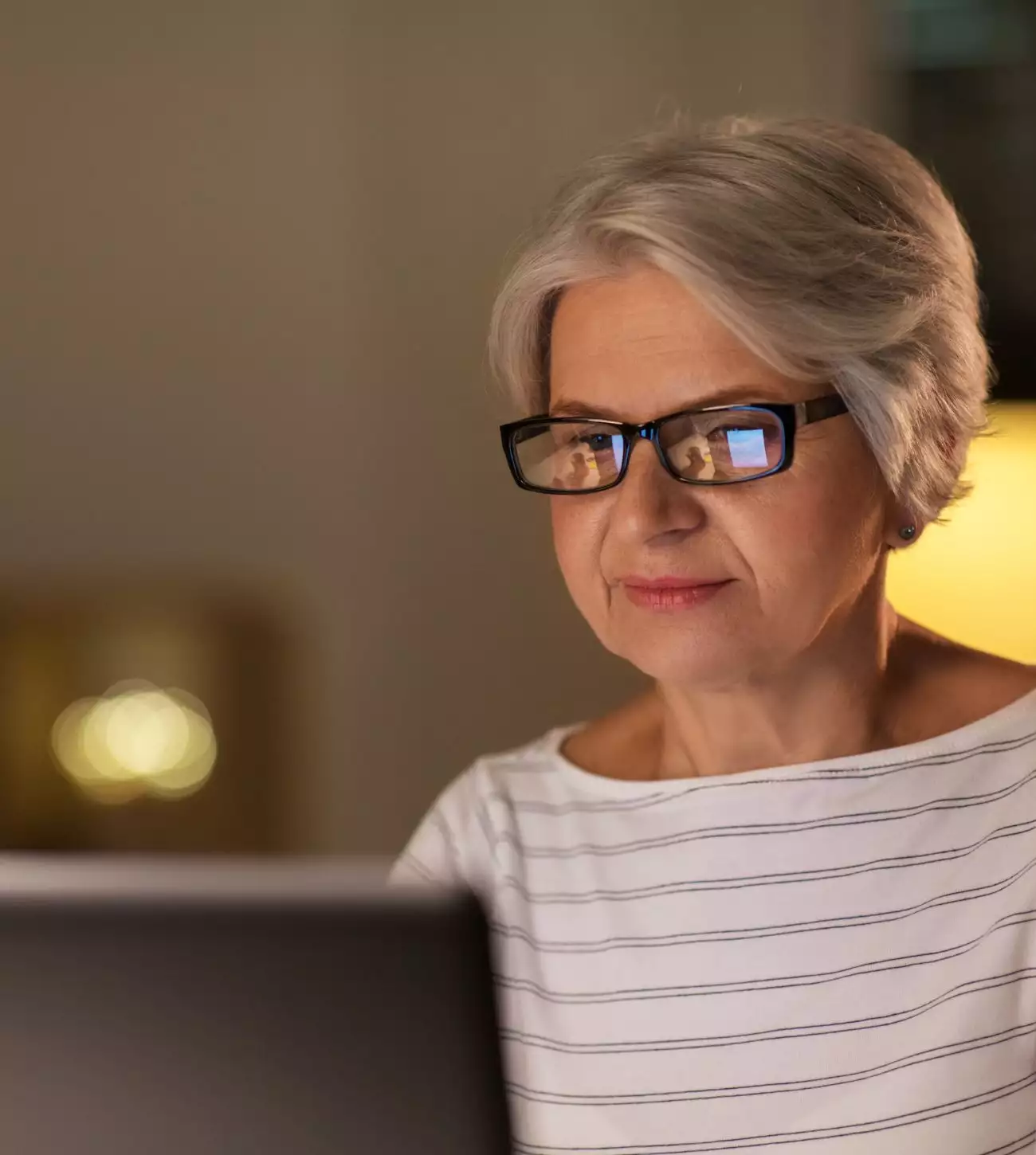 Photo of an older woman working on her laptop in a dimly lit home.