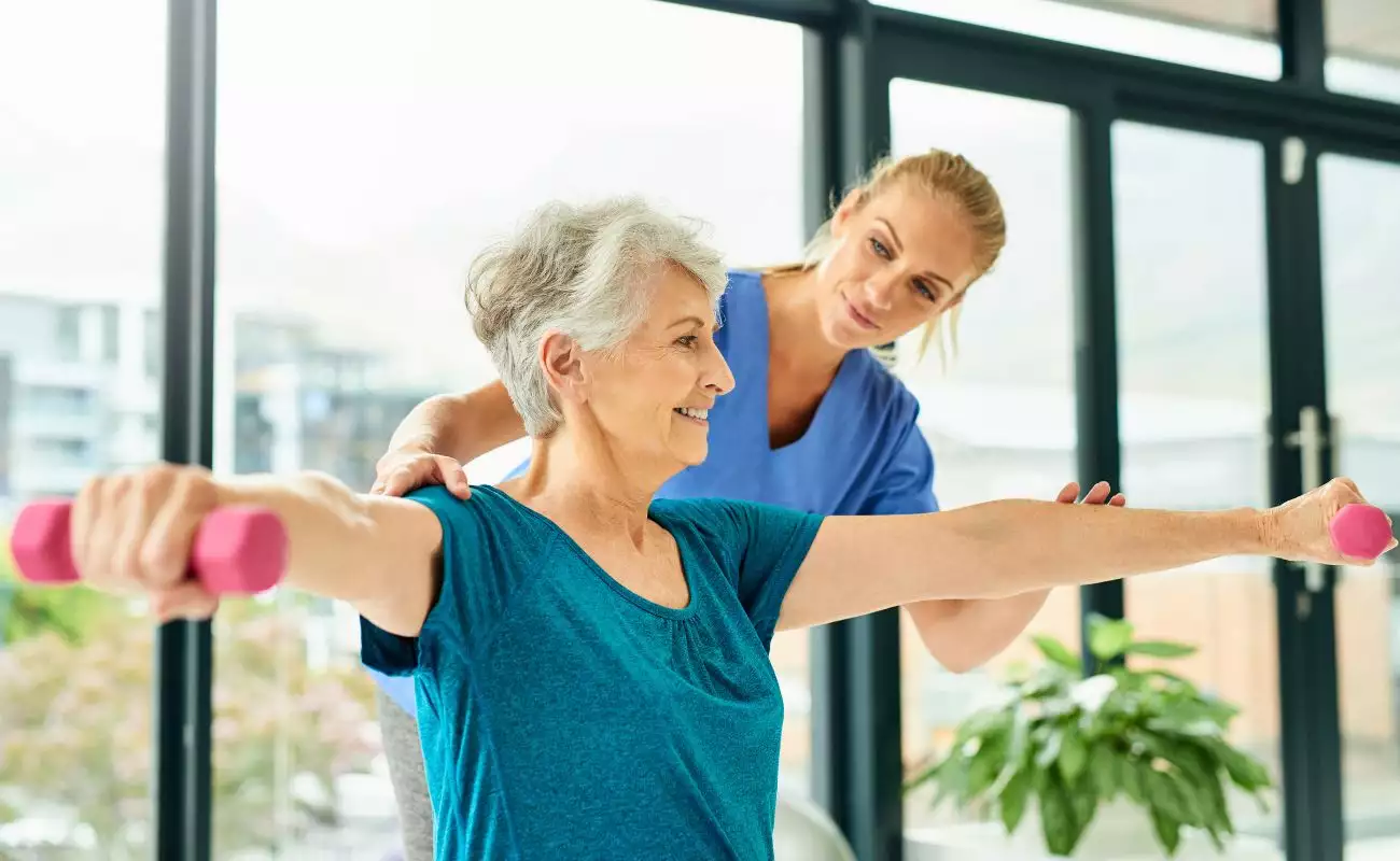 A personal trainer or physical therapist working indoors with a mature woman.