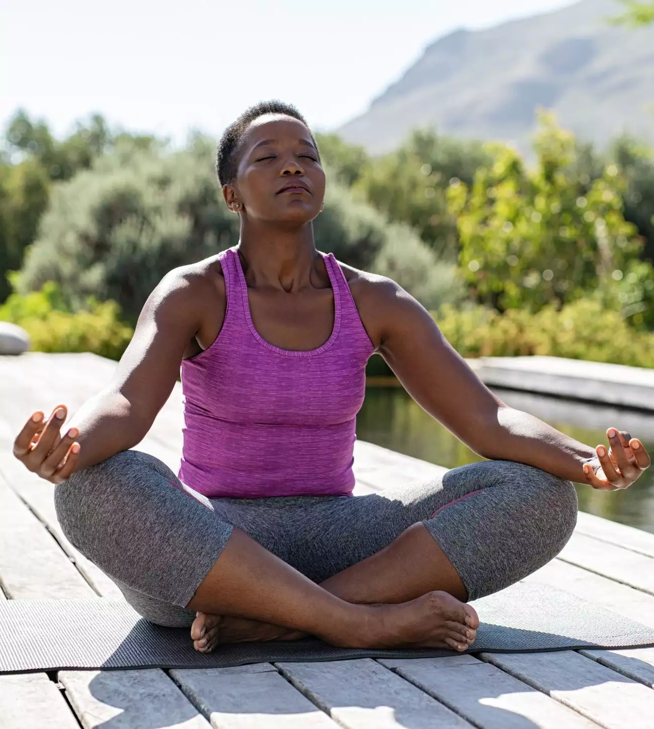 Photo of a middle-aged African American woman in a meditative pose outdoors by a pool.