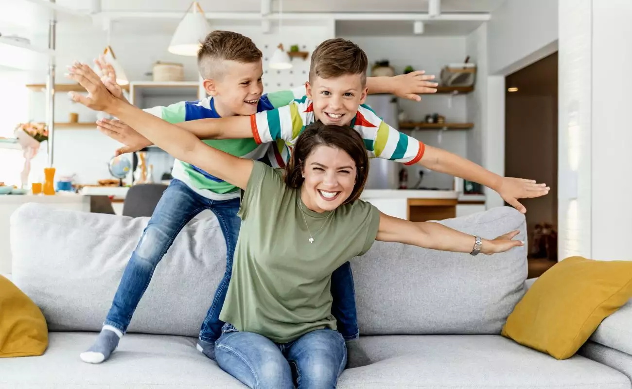 Photo of a young mom horsing around on the couch with her elementary school-aged boys.