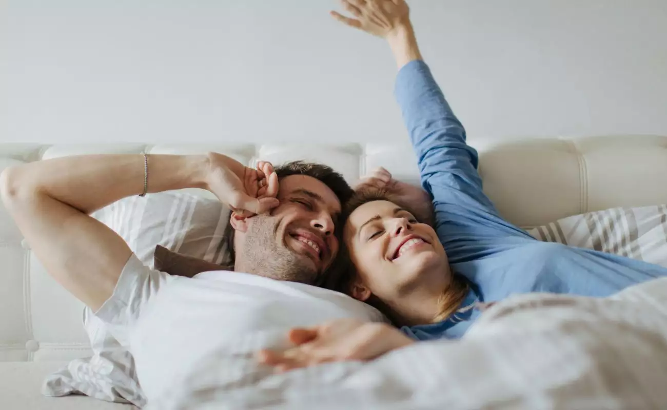 Photo of a younger couple waking up refreshed in the bed.