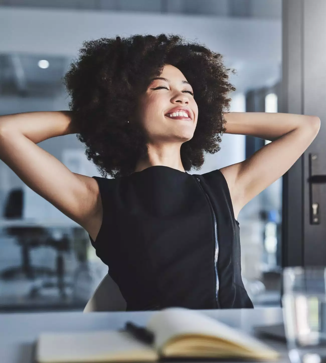 Photo of a young woman smiling and stretching at work.