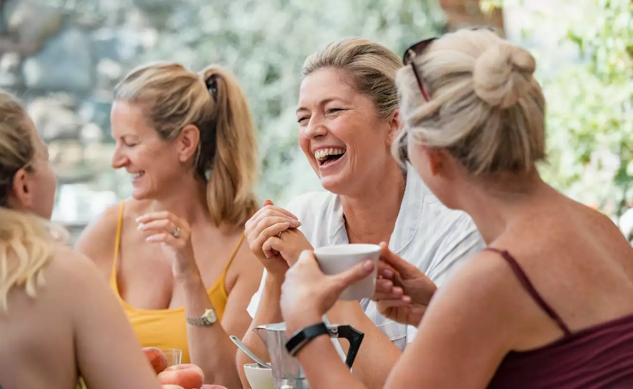 Photo of a group of women gathered and laughing around the table over coffee